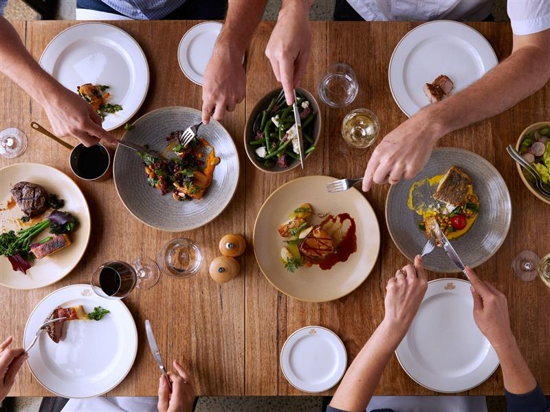 Group of diners from above looking at various plates of food and glasses of wine.