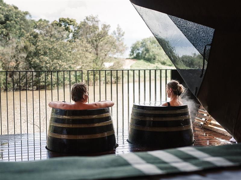 Man and woman bathing in hot springs barrels on their private glamping deck overlooking nature