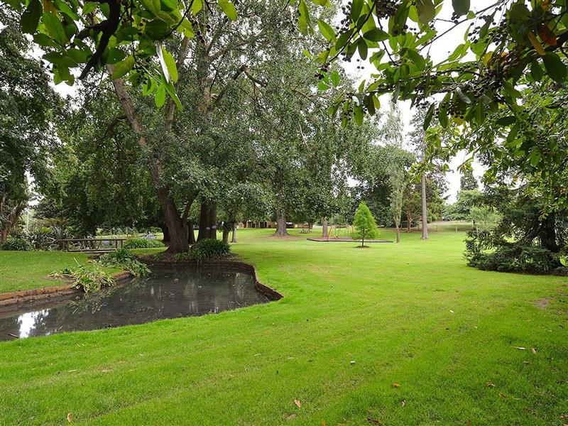 Green garden grounds with small pond to left and playground in far distance
