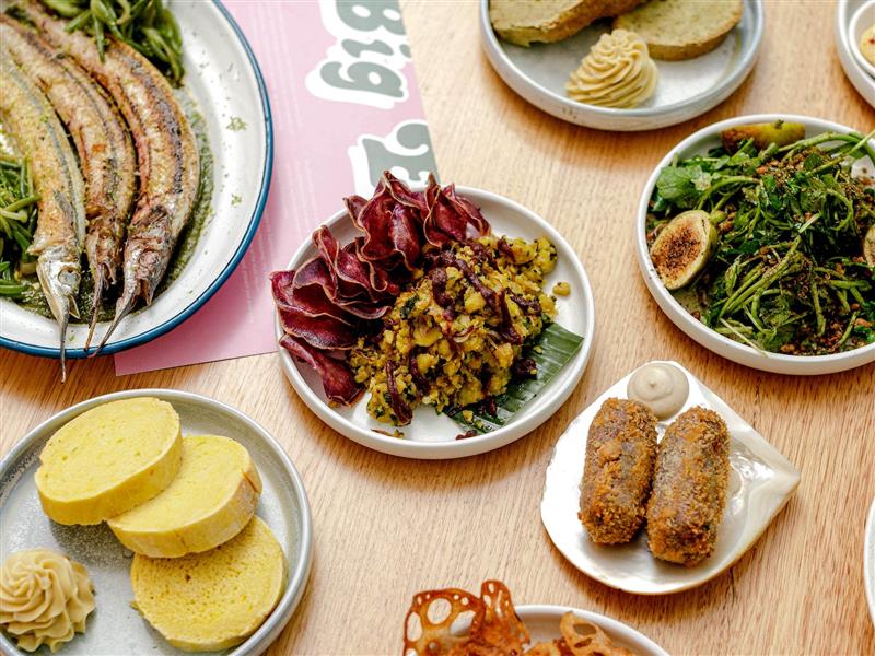 Wooden table with numerous plates of colourful food and pink menu underneath