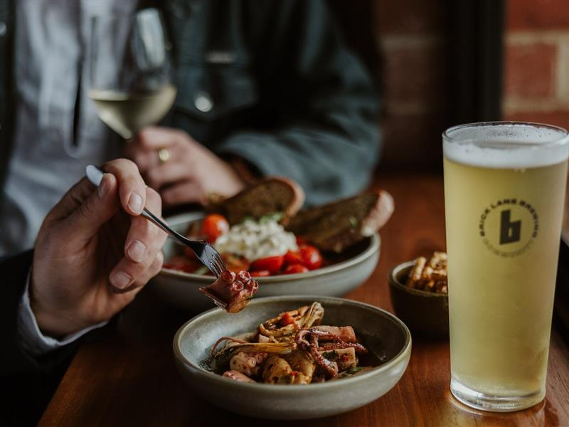 Three bowls, one with pickled octopus, one with salad and bread and last with pretzles next to  beer