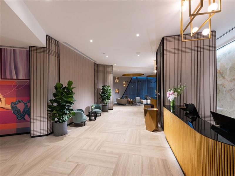 An image of a hotel lobby with artwork, gold reception desks and plants, visibility to the lounge