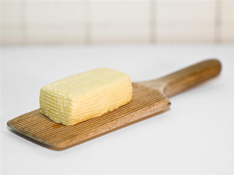 block of yellow butter sitting on a wooden butter paddle