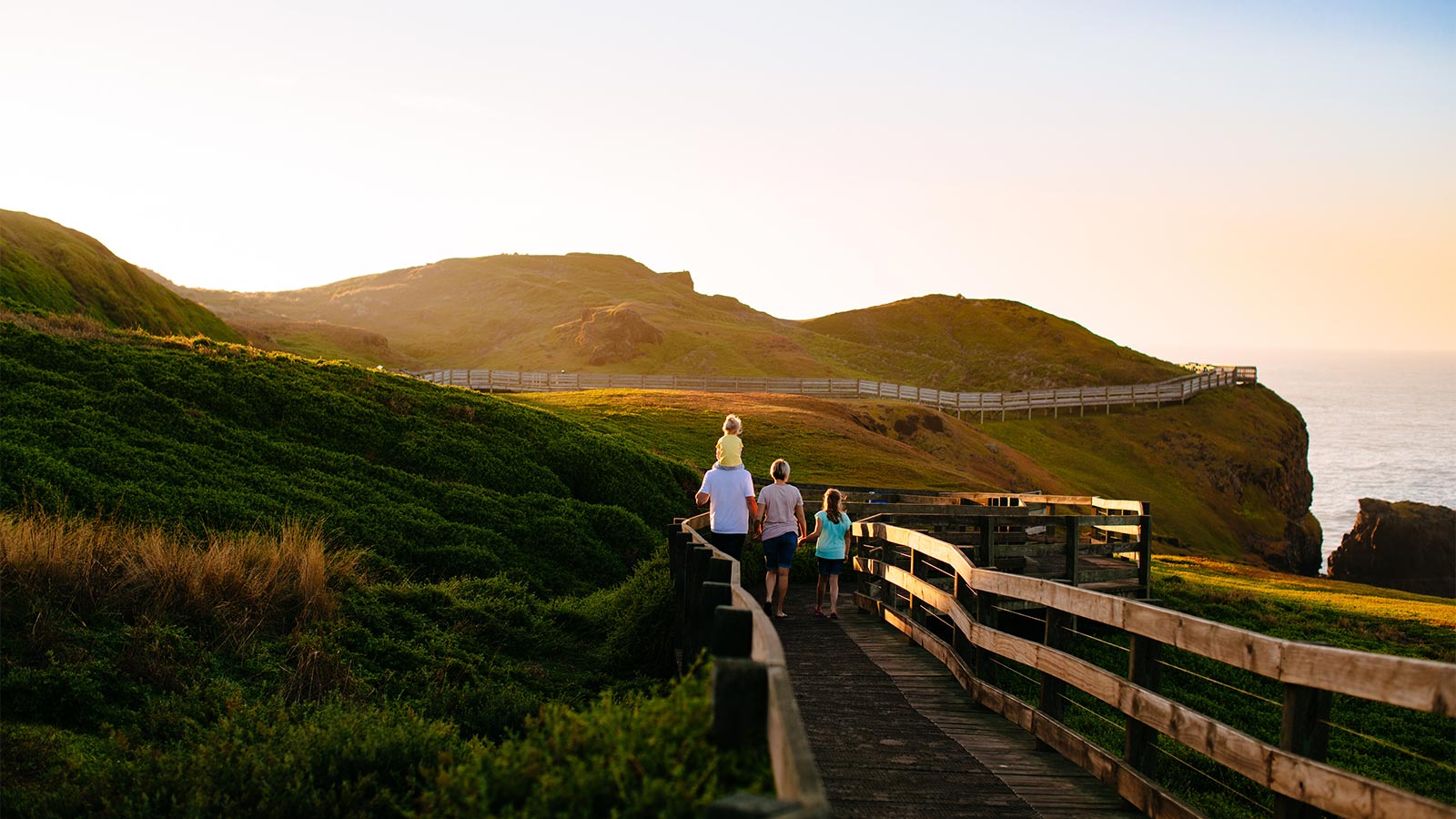 A family walks along the Nobbies boardwalk at sunset